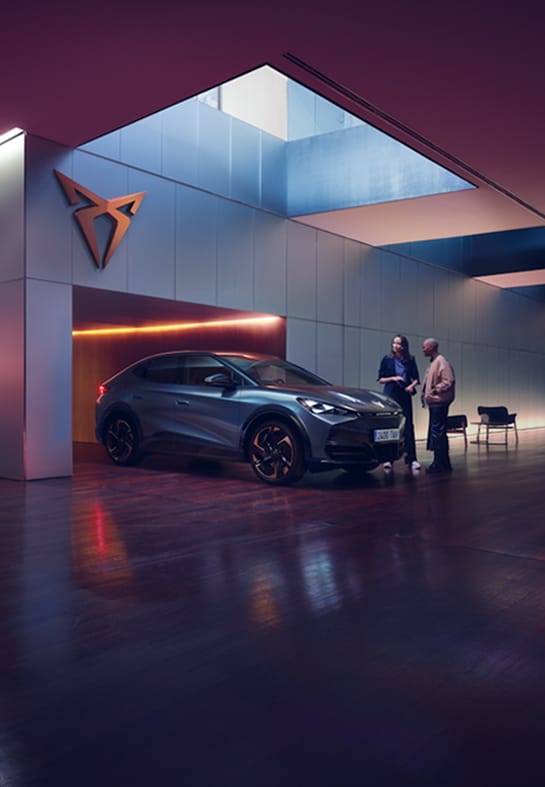 Couple standing in a modern garage with moody lighting looking at a Cupra car