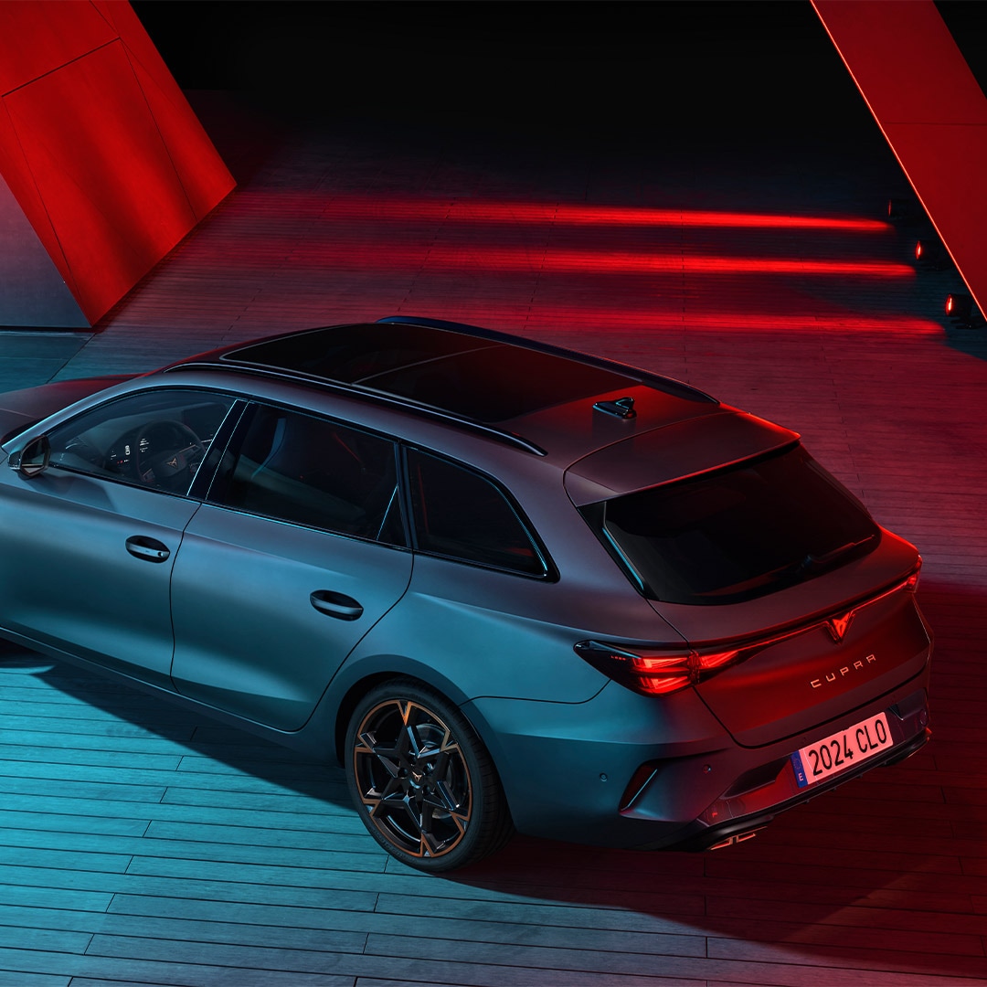 A blue CUPRA car in a surreal scene, superimposed in front of a group of people all facing away except for one man looking back at the viewer. 